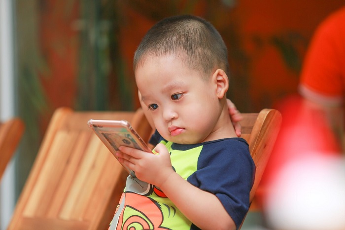 Fotografia. Criança com menos de 5 anos assiste atenta a algum conteúdo no celular.