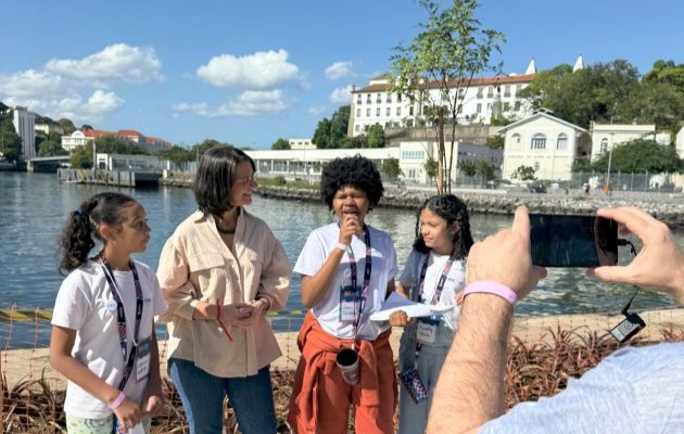 Foto. Três meninas de uniforme escolar entrevista mulher adulta.